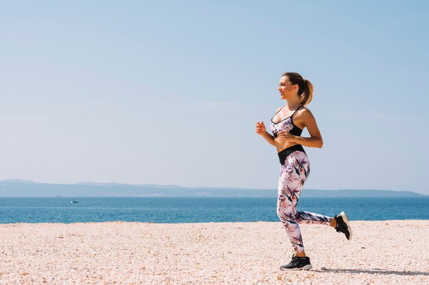 海の近くのビーチで実行されてフィットネスウェアで美しい若い女性