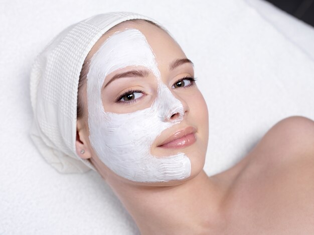 Beautiful young woman getting facial mask at beauty salon - indoors