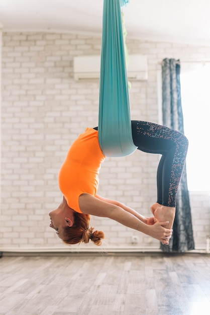 Free photo beautiful young woman hanging upside down while practicing aerial yoga