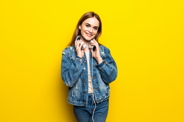 Beautiful young woman in headphones listening to music and dancing on yellow wall