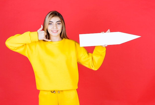 Free photo beautiful young woman holding blank arrow on red wall