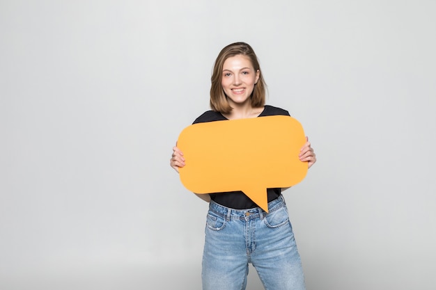 Beautiful young woman holding blank speech bubble over grey wall