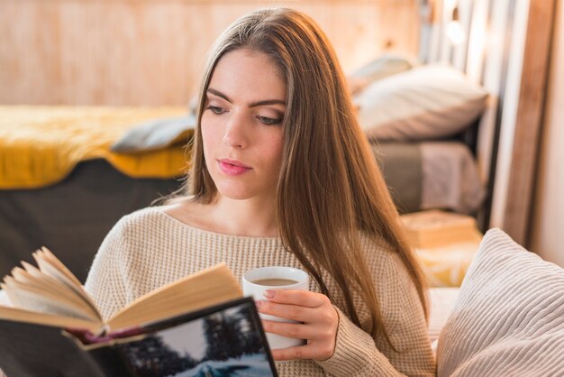 Beautiful young woman holding coffee cup reading book