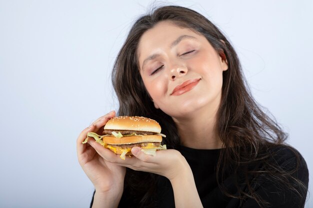 おいしいビーフバーガーを持って空想にふける美しい若い女性。