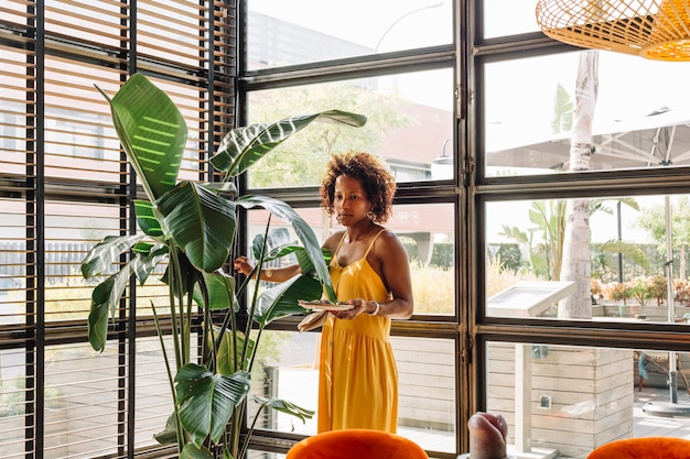 Beautiful young woman holding dish standing near the green plant