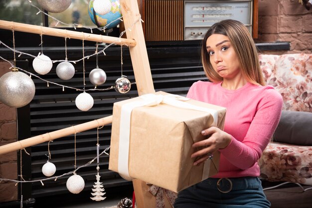 Beautiful young woman holding gift box at home