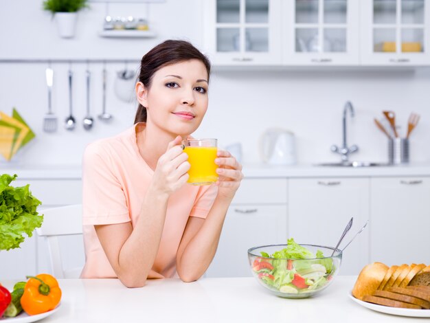 キッチンでオレンジジュースのガラスを保持している美しい若い女性