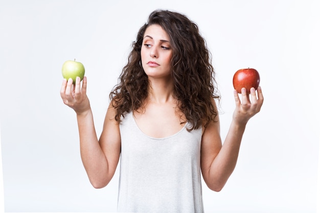 Beautiful young woman holding green and red apples over white background.