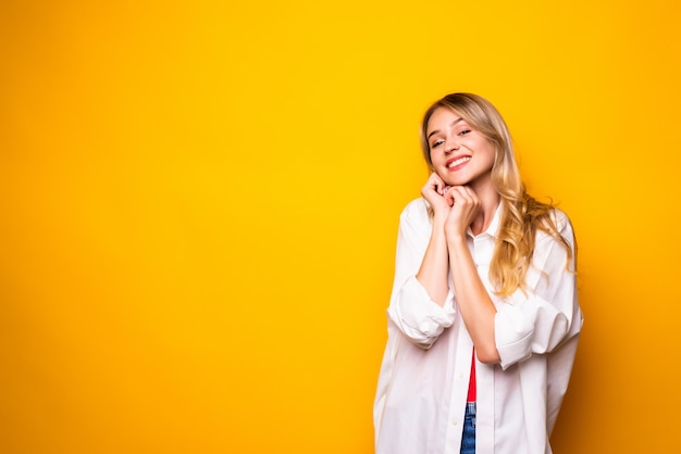Beautiful young woman holding hand on chin, smiling,  on yellow wall.