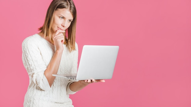 Beautiful young woman holding laptop on pink backdrop