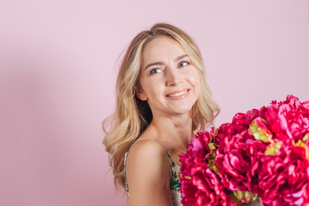 ピンクの背景に対してバラの花束を保持している美しい若い女性