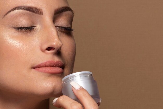 Beautiful young woman holding skin care product