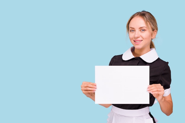 Beautiful young woman holding white blank paper and presenting against blue backdrop