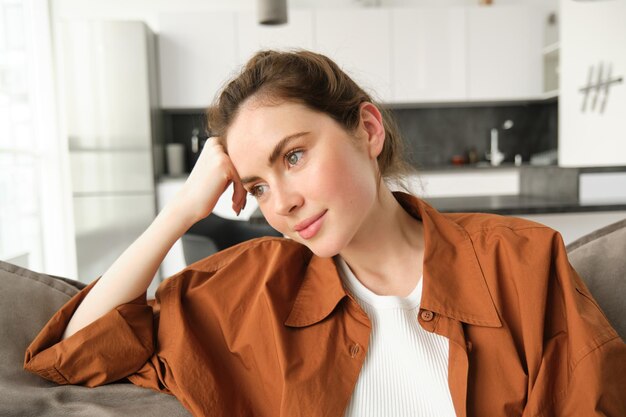 落ち着いた ⁇ 細な顔で窓の外を見つめるソファーに座っている美しい若い女性