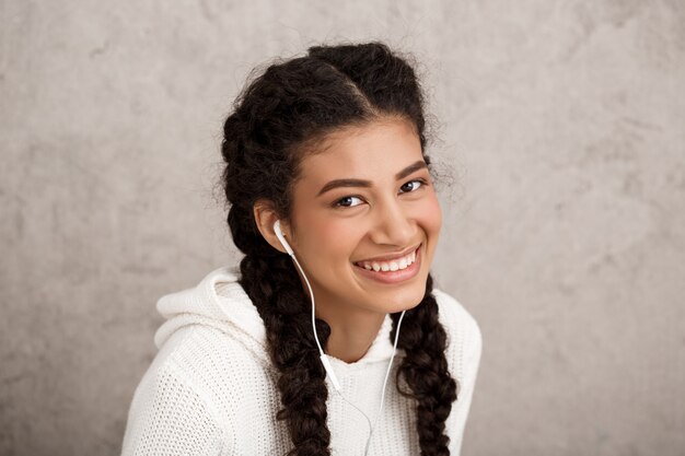Бесплатное фото Красивая молодая женщина в наушниках, улыбаясь на бежевой стене