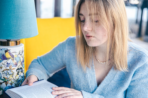 Beautiful young woman is reading a book while sitting at the table