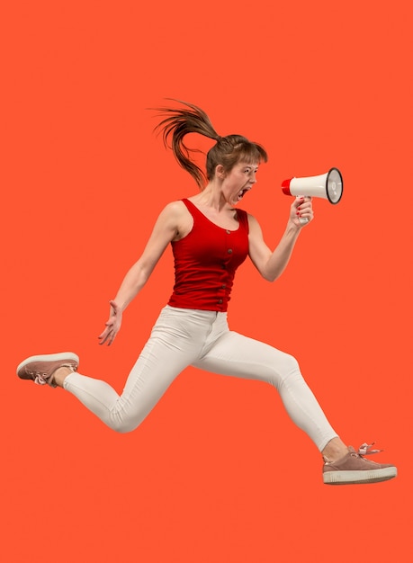 Beautiful young woman jumping with megaphone isolated over red