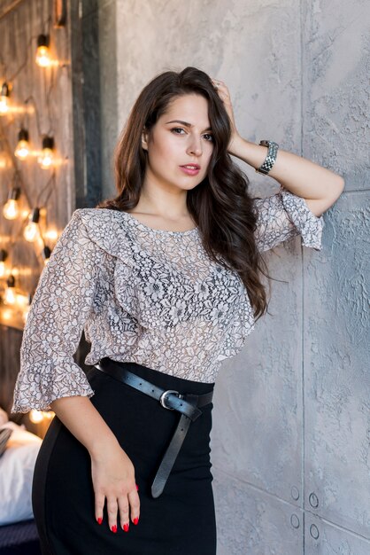 Beautiful young woman leaning on grey wall looking at camera