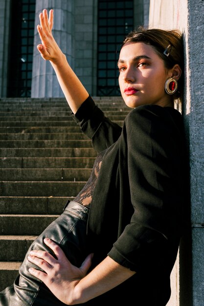 Beautiful young woman leaning on wall shielding her eyes from sun