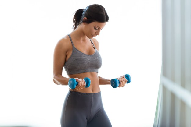 Beautiful young woman lifting dumbbells at home.