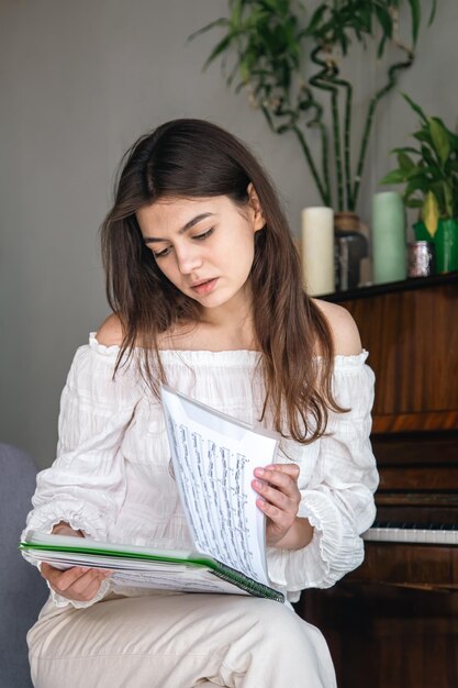 A beautiful young woman looks at the notes while sitting near the piano