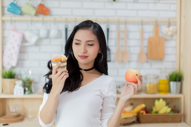 Beautiful young woman making a choice between a cake and apple