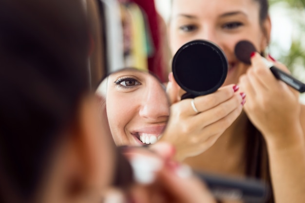 Bella giovane donna che fa trucco vicino allo specchio a casa.