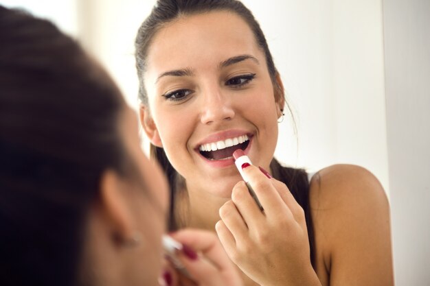 Beautiful young woman making make-up near mirror at home.
