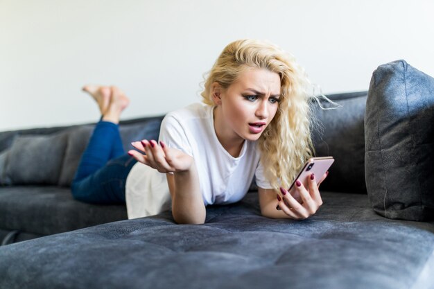 Beautiful young woman making selfie by smart phone while lying on couch at home