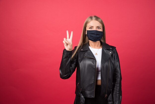Beautiful young woman in a medical face mask showing victory sign