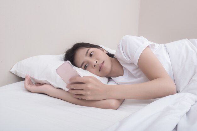 Красивая молодая женщина, играя телефон на кровати в первой половине дня