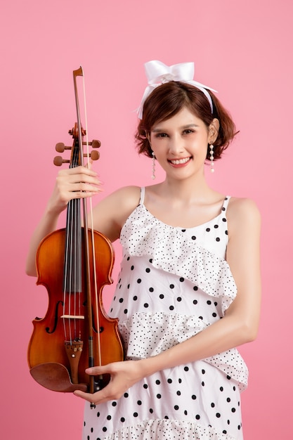 Beautiful young woman playing violin over pink