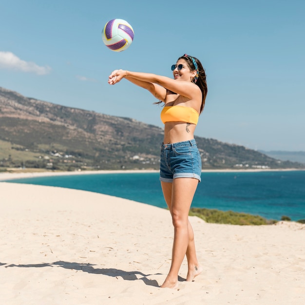 Bella giovane donna che gioca a pallavolo sulla spiaggia