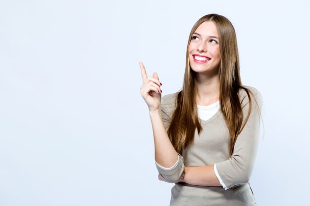 Beautiful young woman pointing up over white background.