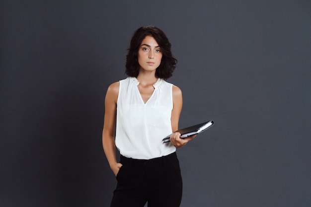 Beautiful young woman posing over grey wall and holding notebook in hands