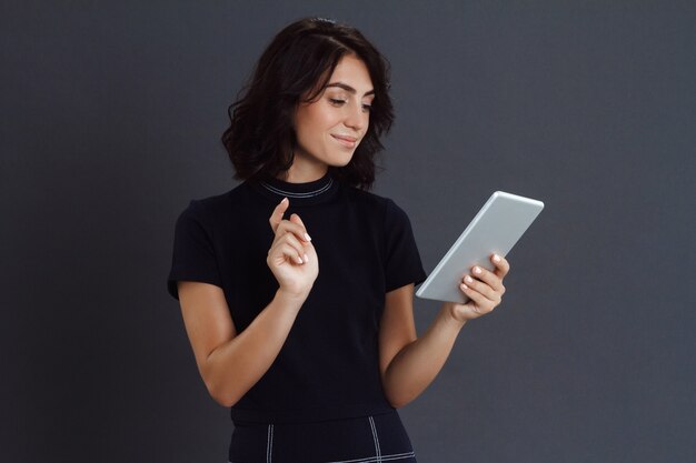 Beautiful young woman posing over grey wall and holding tablet in hands