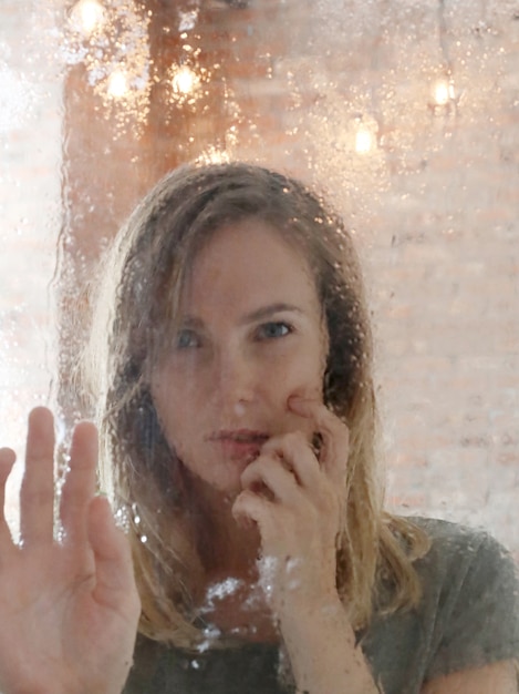 Beautiful young woman posing behind wet window