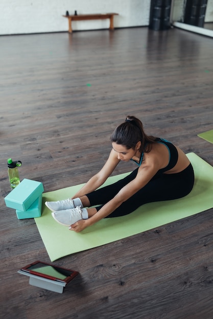 Beautiful young woman practicing yoga, is engaged with the teacher online via a tablet. Home sports concept.