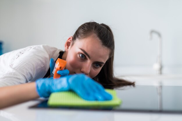 Beautiful young woman in protective gloves cleaning oven with rag