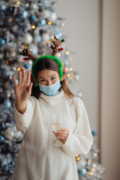 Beautiful young woman in protective mask with glass of champagne