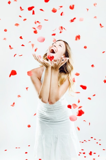 Bella giovane donna sotto una pioggia di petali di rosa. isolato su bianco.