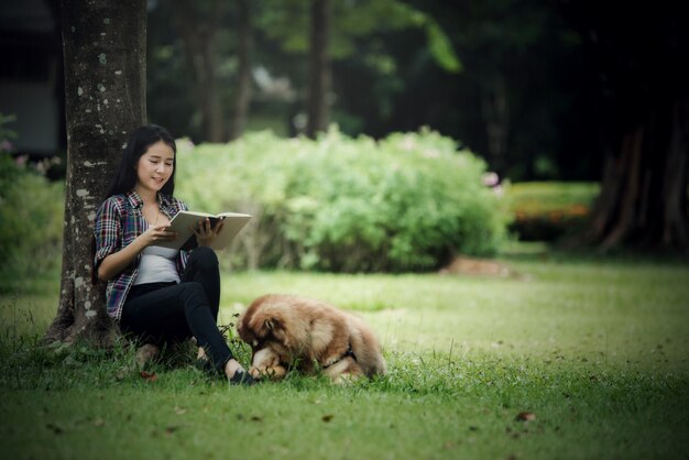 屋外の公園で彼女の小さな犬と一緒に本を読んで美しい若い女性。ライフスタイルの肖像画。