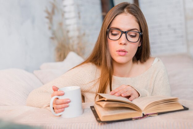 Beautiful young woman reading book with white cup in hand