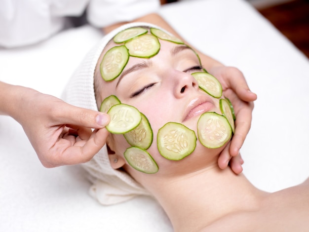 Beautiful young woman receibing facial mask of cucumber in beauty salon