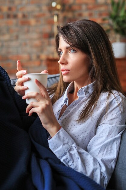 温かい飲み物とソファでリラックスした美しい若い女性