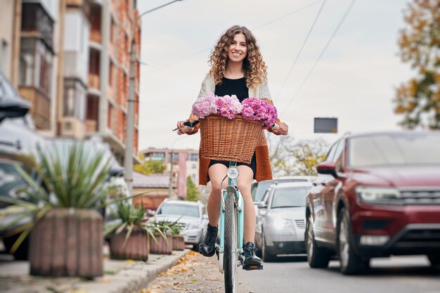 Beautiful young woman riding bicycle with flowers on the street