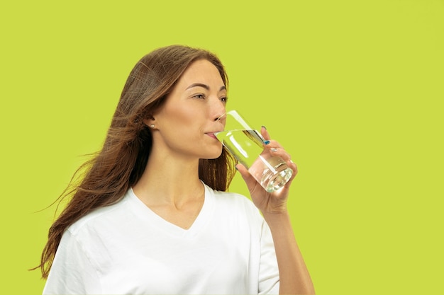 Beautiful young woman's half-length portrait isolated. Female model looks happy and drinking water. Facial expression, human emotions concept, beauty and healthcare.