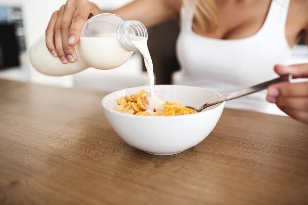 ボトルを押しながらボウルに牛乳を注ぐ美しい若い女性の手