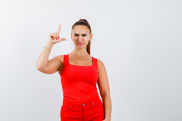 Beautiful young woman showing gun gesture in red tank top and looking serious. front view.