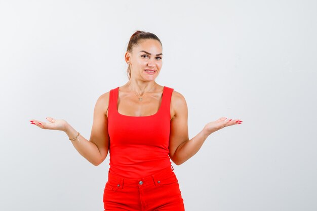 Beautiful young woman showing helpless gesture in red tank top and looking confused. front view.